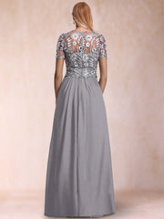A woman shown from the back wearing a floor-length gray gown with a heavily embellished lace and bead bodice and short sleeves, against a soft beige studio backdrop.