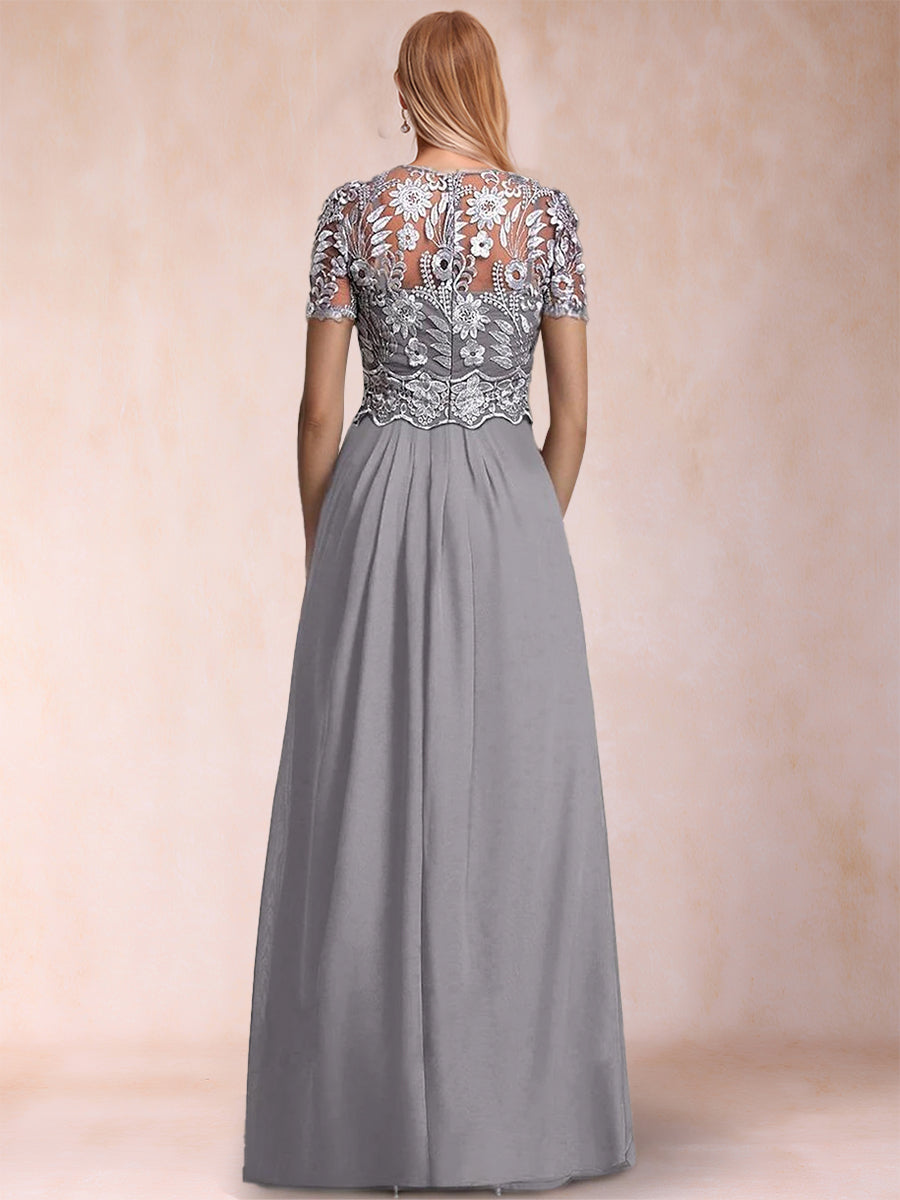 A woman shown from the back wearing a floor-length gray gown with a heavily embellished lace and bead bodice and short sleeves, against a soft beige studio backdrop.